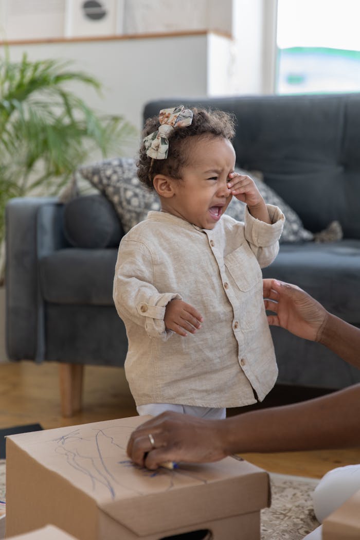 A young child crying in a living room with comforting surroundings, depicting emotion and family life.