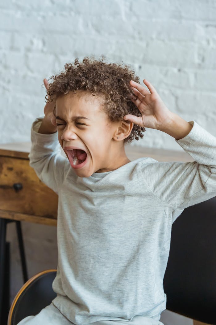 Young black child showing frustration in an indoor setting, hands on head in distress.
